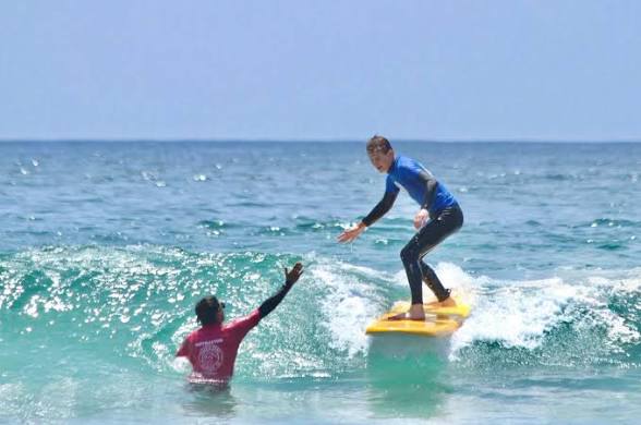 A beginner standing up on a soft-top surfboard on a small wave at Tourmaline